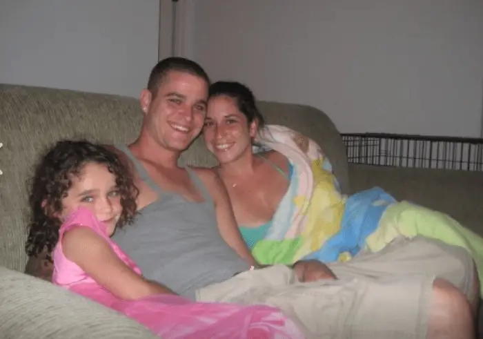 Tyler Darnell smiles while sitting on couch with girlfriend and daughter.
