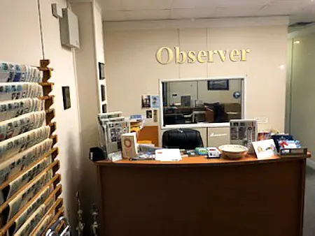 cluttered desk, black chair in front of a wall with "Observer" sign