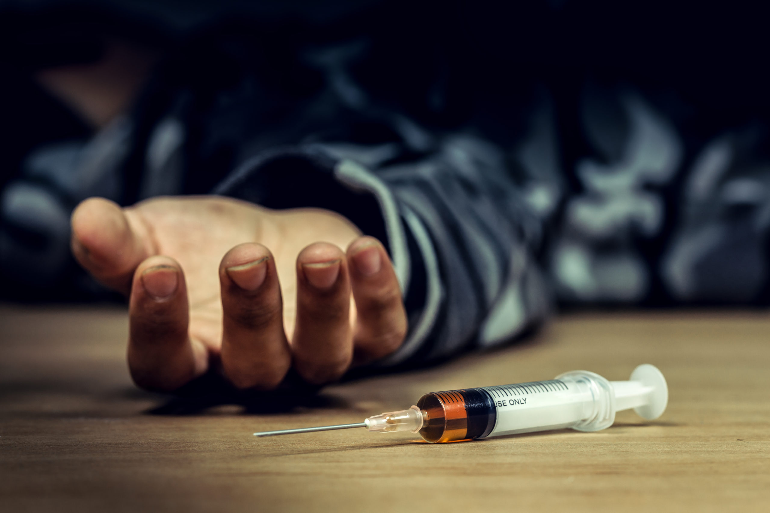 a syringe lying next to a dead man's outstretched hand