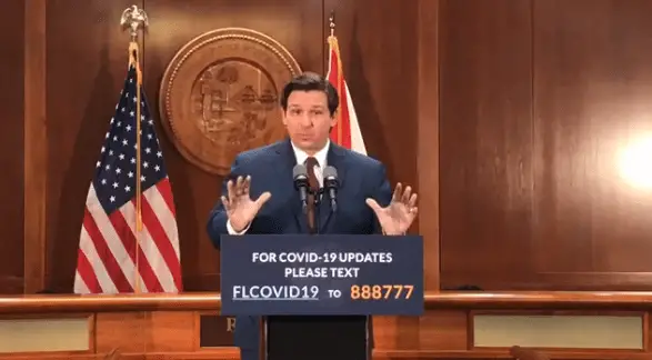 gov. ron desantis standing in front of flags and wood paneled walls making an announcement on April 22.